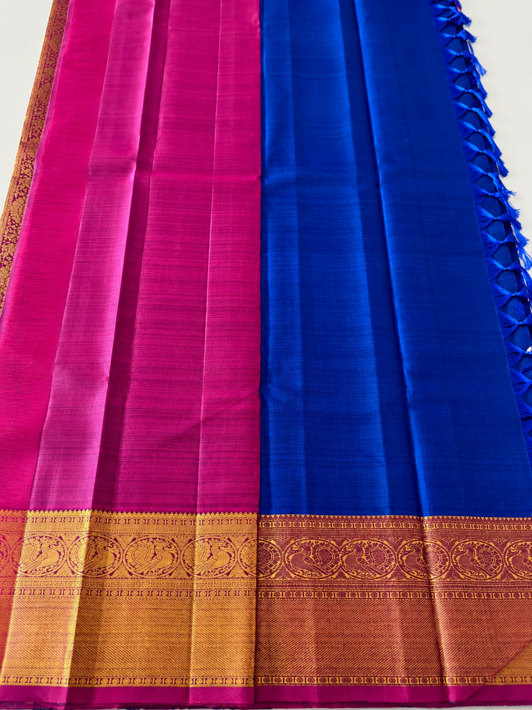 Pure Kanjivaram silk in regal royal MS blue, adorned with traditional gold motifs, an intricate zari border and a striking magenta edge. Silk Mark Certified.