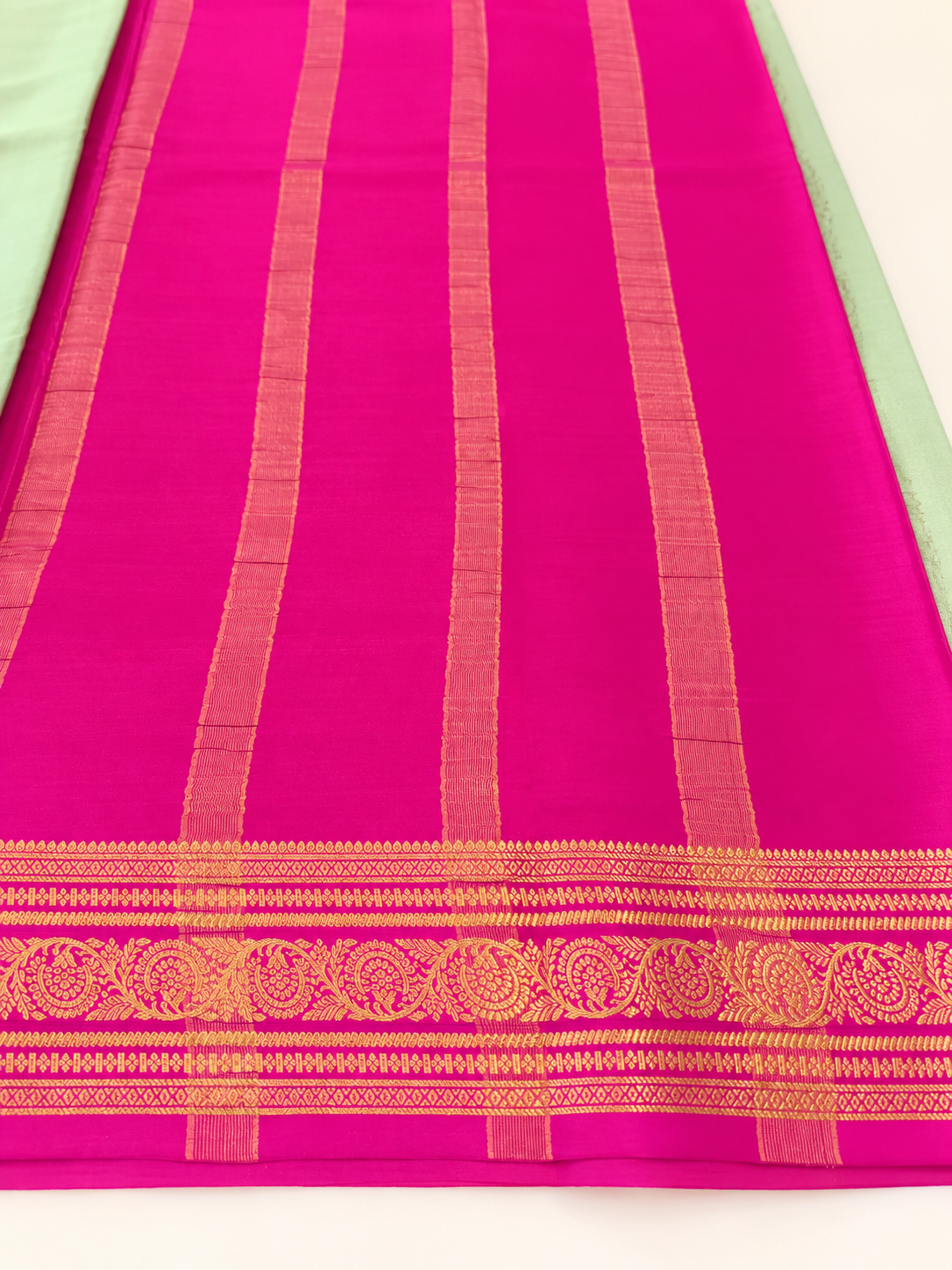 legant pastel green Pure Mysore Silk Crepe with a vibrant Rani Pink pallu and intricate floral gold zari borders.