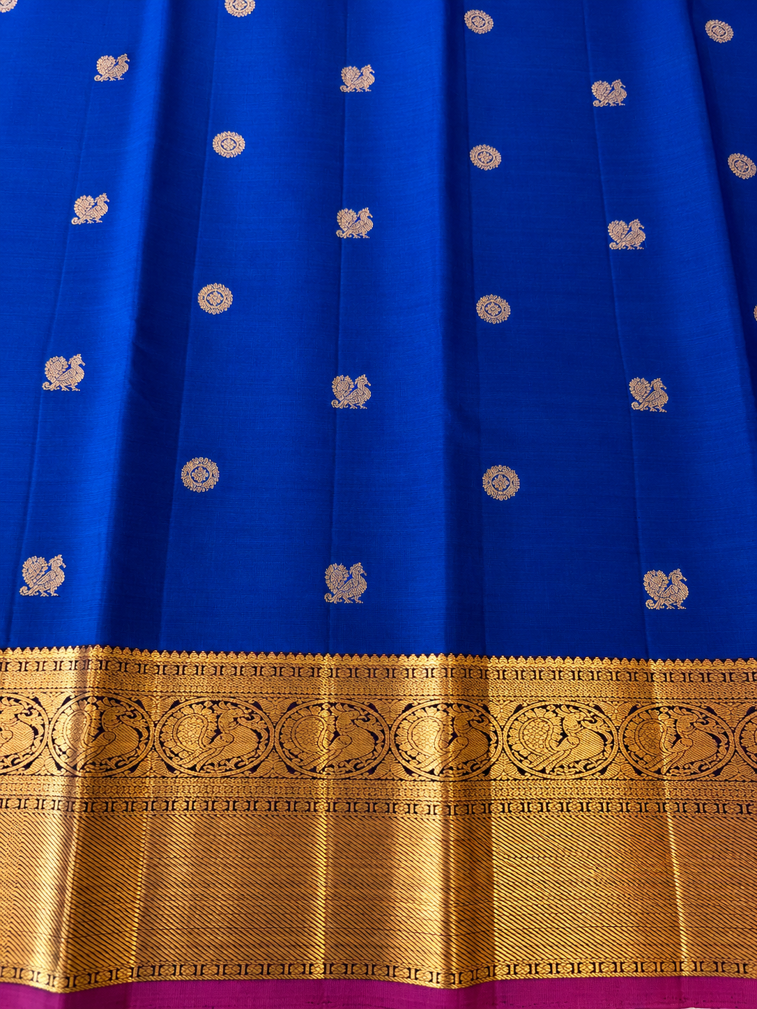 Pure Kanjivaram silk in regal royal MS blue, adorned with traditional gold motifs, an intricate zari border and a striking magenta edge. Silk Mark Certified.