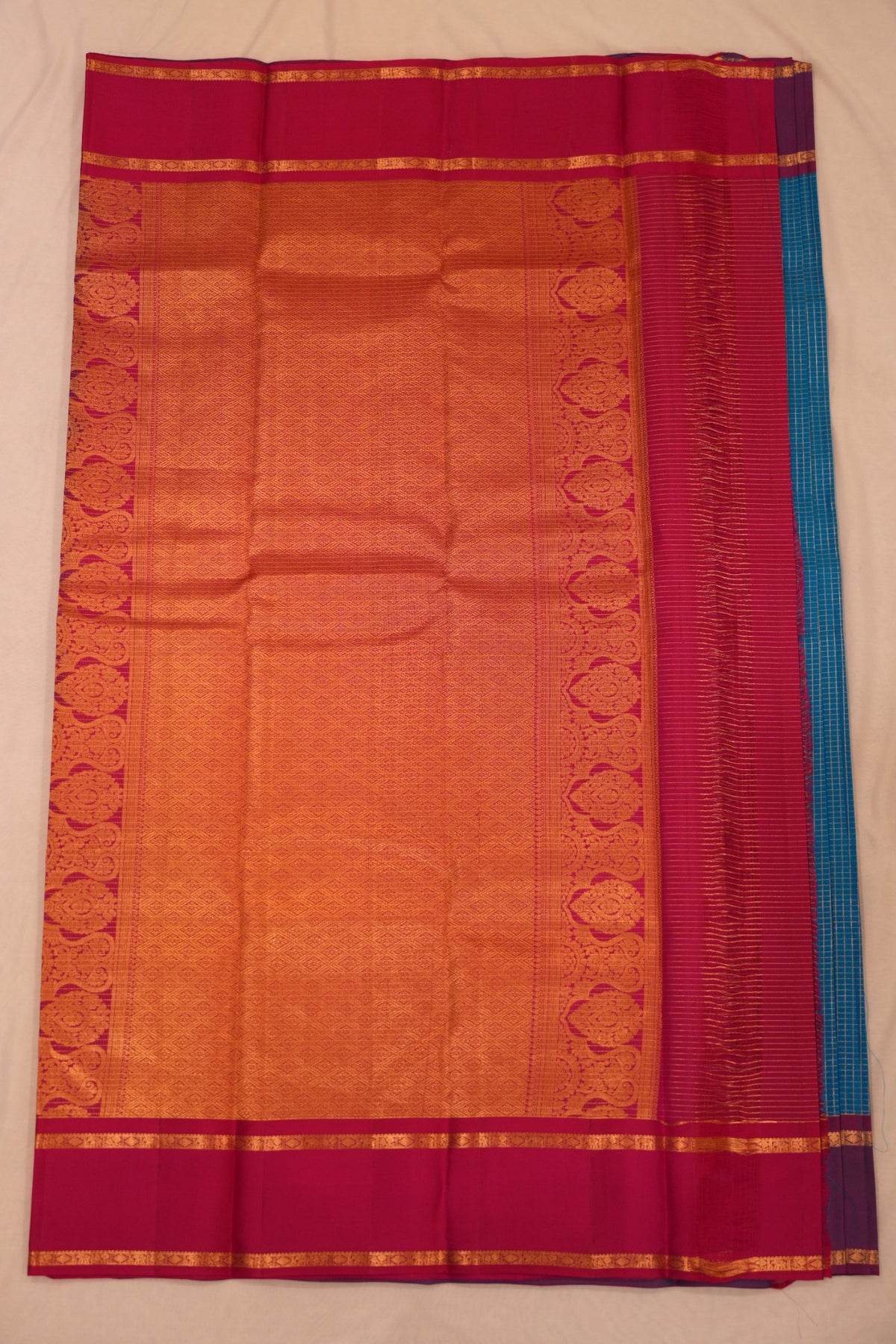 Vibrant turquoise blue Kanjivaram silk with gold zari checks and leaf motifs, complemented by magenta and a traditional elephant, peacock & diamond zari border.