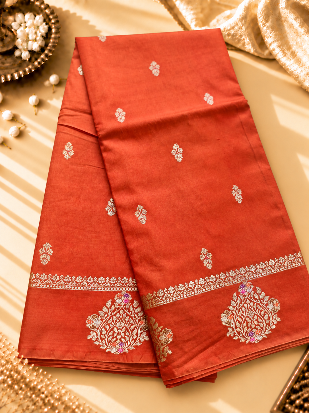 A vibrant Coral Orange Banarasi viscose silk saree featuring delicate traditional butis, intricate floral motifs and elegant Minakari weaving. The warm coral-orange base beautifully complements the metallic and colourful detailing,