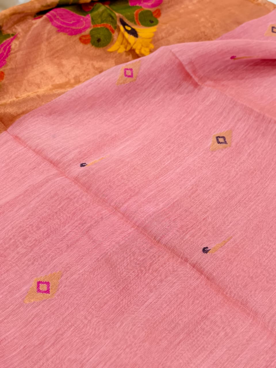 Elegant pastel pink Tissue Linen Jamdani saree with Paithani-style handwoven parrot motifs and delicate golden zari detailing.