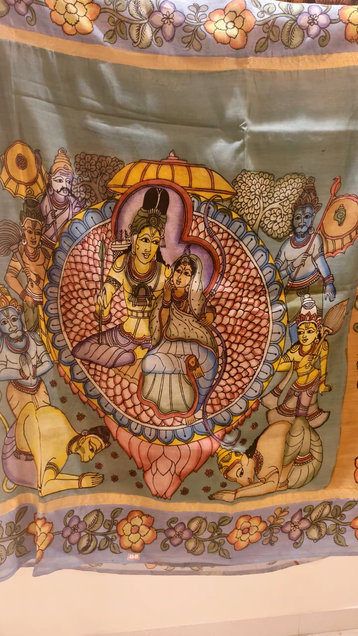 Hand-painted Kalamkari saree in Bangalore Silk featuring Rama & Sita on the body, Krishna & Radha on the pallu, floral borders, and a matching lavendar lotus-motif blouse piece